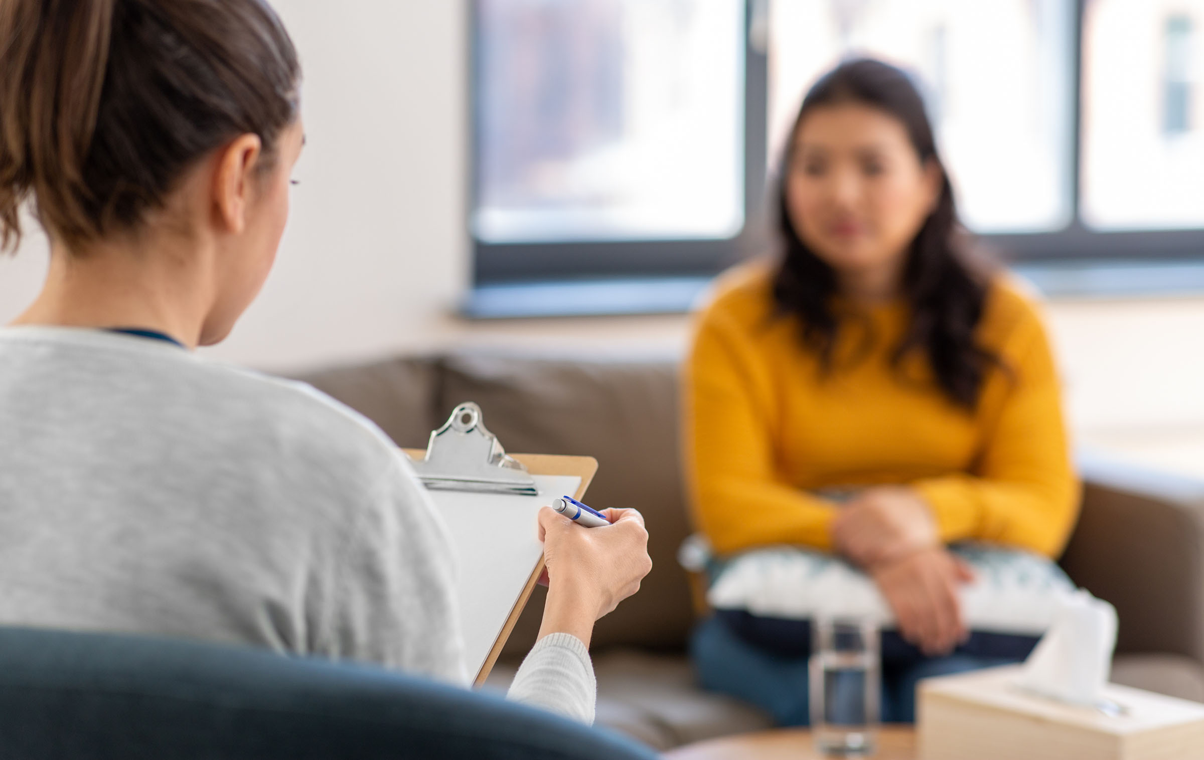 woman at desk with clipboard talks to another woman